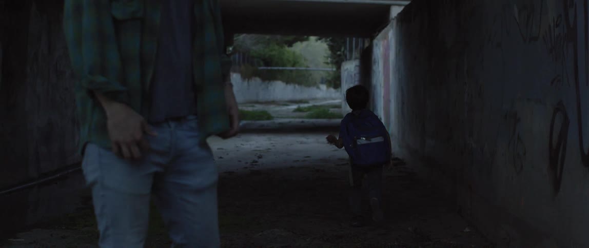 A man motions for a boy to leave while standing under a bridge