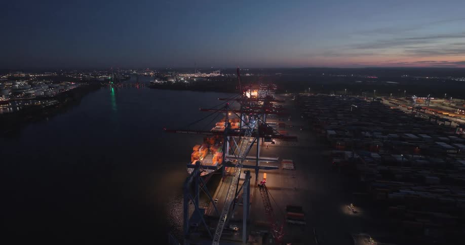 Port operating at night with illuminated cranes and aligned containers along the riverside