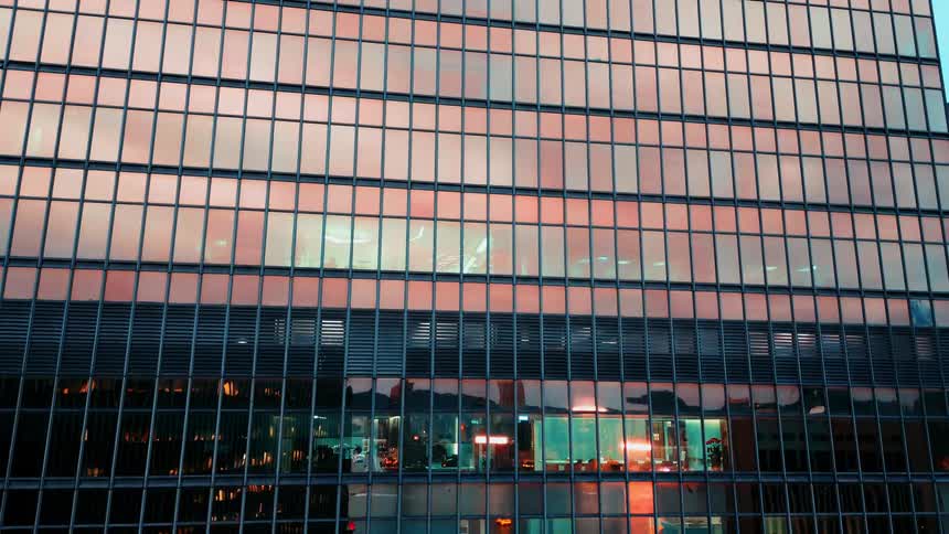 Urban reflection on glass facade at dusk reveals mosaic of city lights and architecture