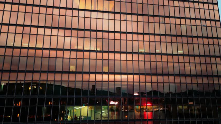 Glassfronted office building reveals lit workspaces across multiple floors during nighttime