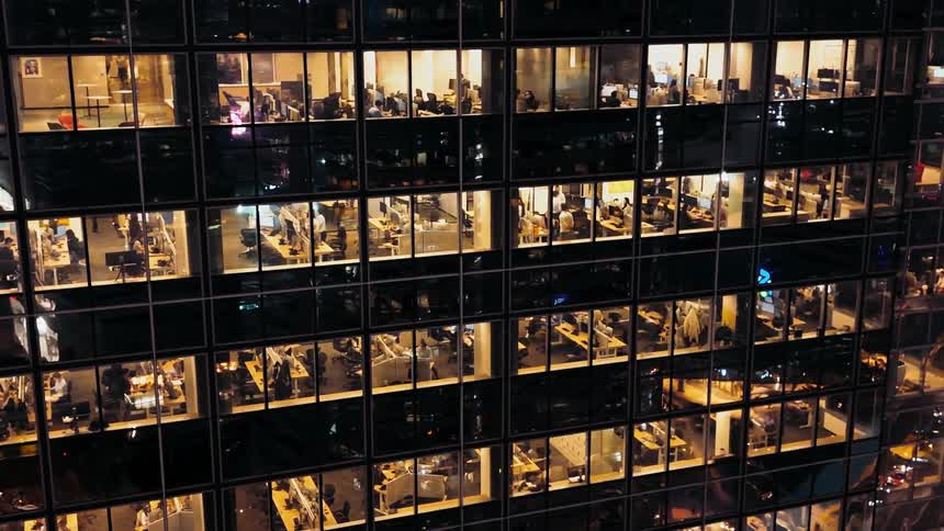 A modern high rise office building facade with employees working inside at night