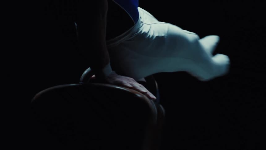 Close up of a male gymnast performing moves in a dark room