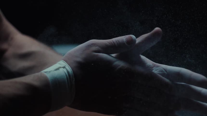 Close up of a male gymnast applying chalk to their palms while sitting in a dark room