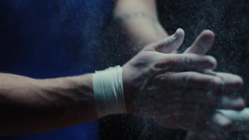 A closeup shot captures the hands of an athlete vigorously clapping chalk together creating a cloud of white powder that sprays around them the person is preparing for a strenuous activity possibly gymnastics or weightlifting with their wrists taped