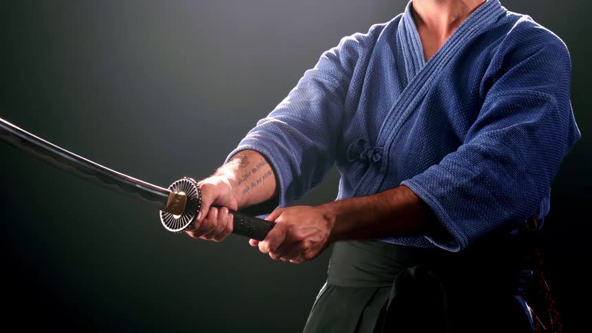 A young man in a japanese fighting stance with a sword in a dark room