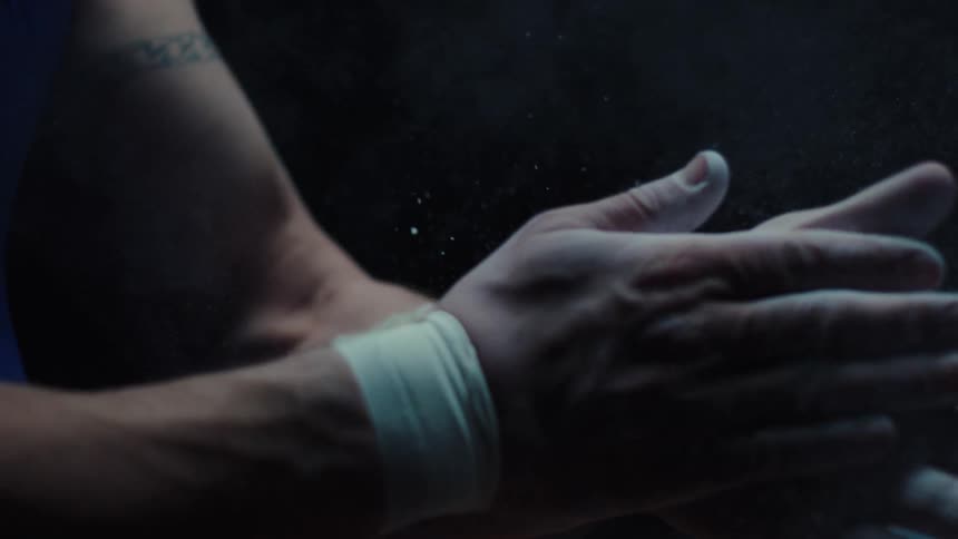 Close up of a male gymnast applying chalk to his palms while sitting in a dark room