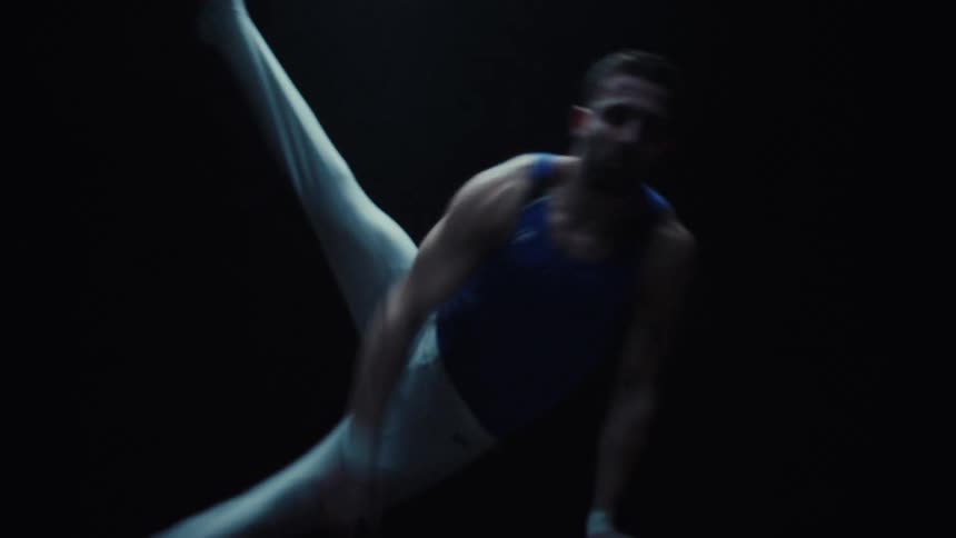 A male gymnastics athlete spins on a wooden bar holding the handle while wearing tights
