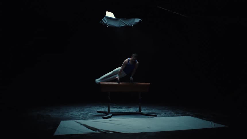 Gymnast training on the pommel horse under a beam of light in a dark setting