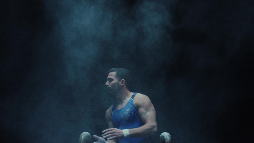 Gymnast clapping hands with magnesium chalk dispersing in the air above the pommel horse