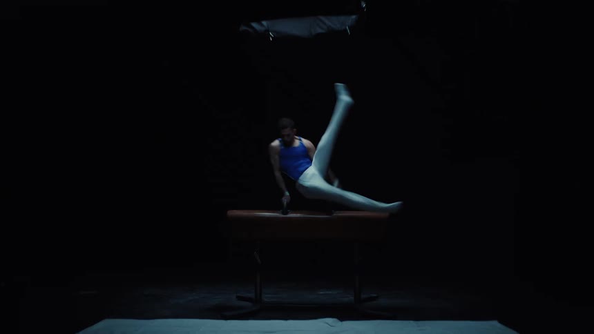 Gymnast performing moves on the pommel horse in a dark setting