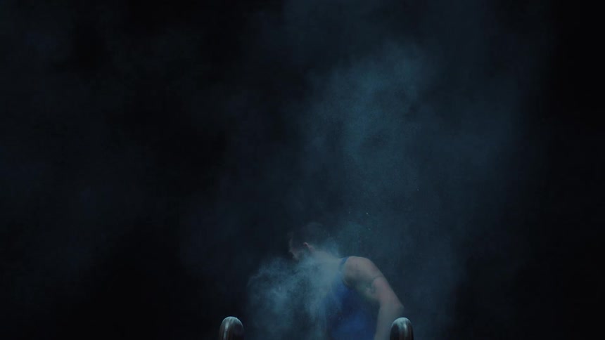 Gymnast dispersing magnesium chalk in the air in front of the pommel horse
