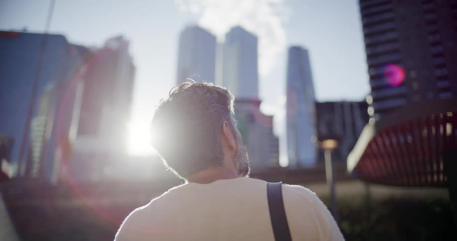 A man looks up at several tall skyscrapers on a sunny day