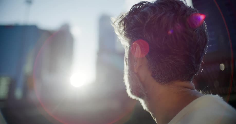 Man looking toward the city with sunlight lens flare behind his head