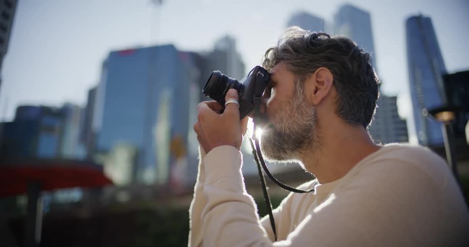 Man framing a photo with a camera in front of sunlit buildings