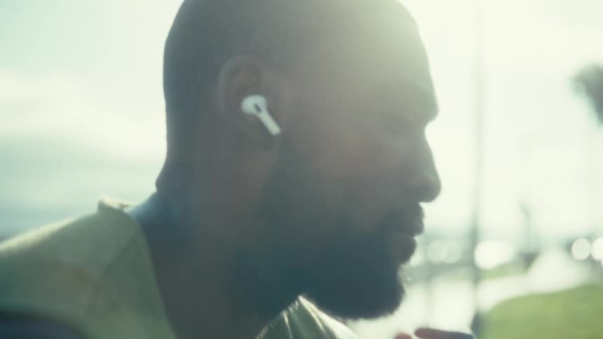 Man sitting outside on a bench wearing an earpiece as he holds his phone