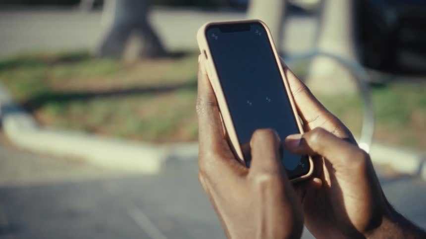 A person standing outside on a sunny day texts using their smart phone