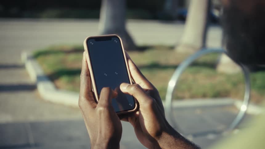 Bearded man standing in a parking lot during the daytime texts on a smartphone
