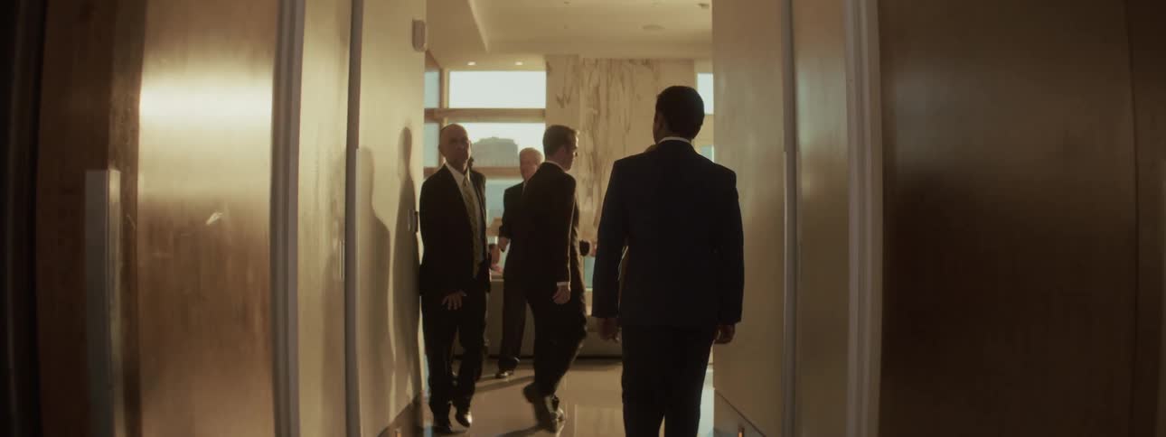 Professionals in suits walking through a narrow hallway toward a lit room