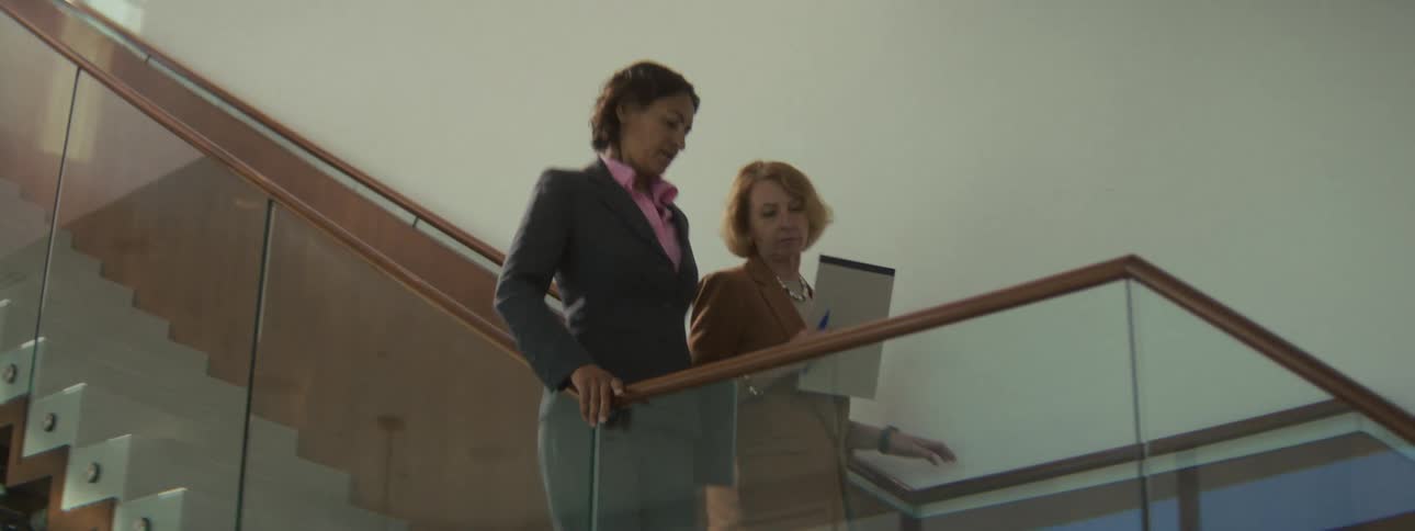Two women in business attire walk down a flight of stairs will conversing