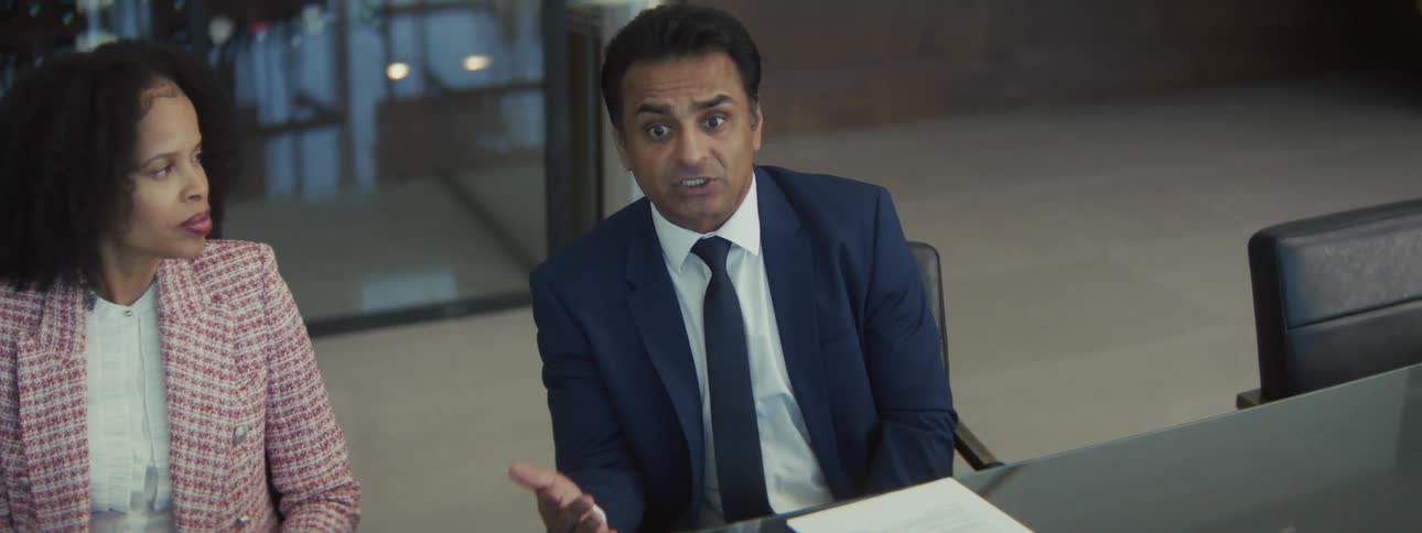 Adult man wearing a suit and tie talking to other people and showing them a smartphone in a business meeting indoors during day time