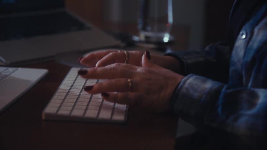 A woman wearing glasses types on a keyboard beside a tablet displaying code and data analytics