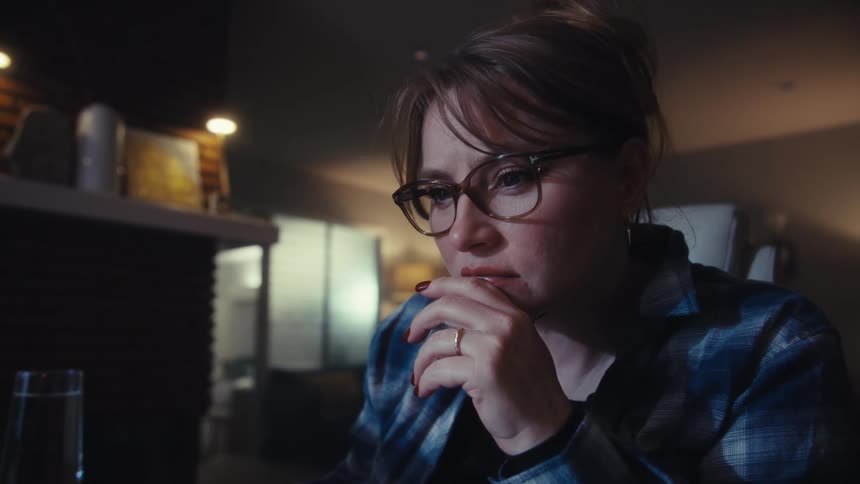 Young adult woman wearing glasses and a blue plaid shirt reading on a computer at a destk indoors during day time