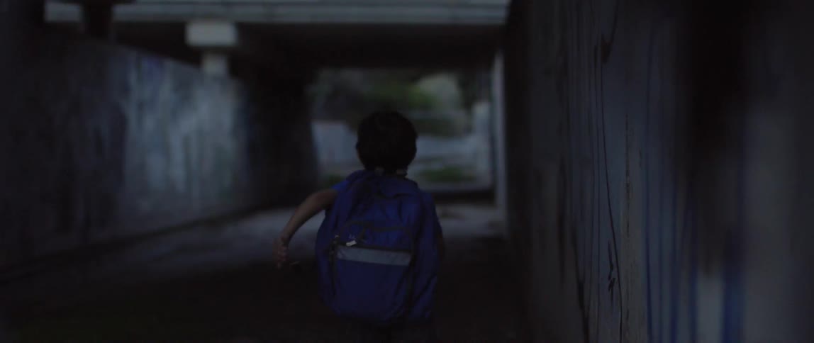 A young boy stands outside watching something and then runs under a bridge