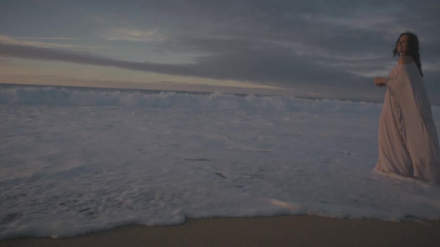 Woman walking on the wet shoreline by the sea at dusk
