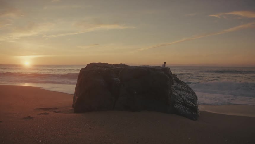 Person sitting on a large rock on the beach during sunset