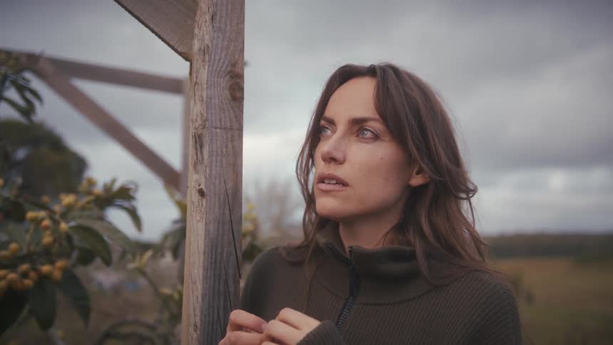 Woman standing beside a wooden structure in an outdoor area