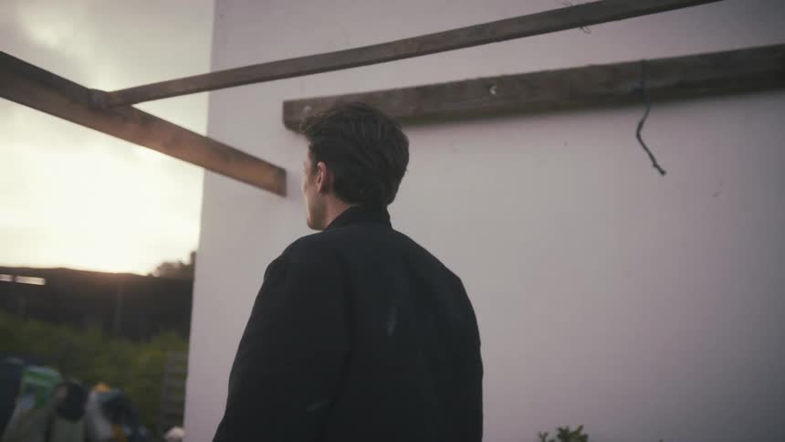 A young man stands beside a building at midday contemplating as he walks to and fro with sadness