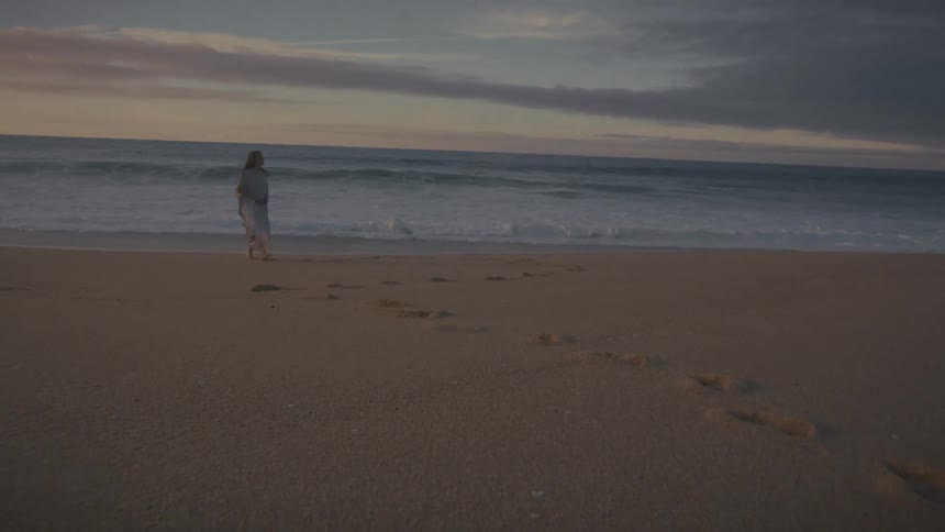 Footprints in the sand lead to a woman walking on the beach