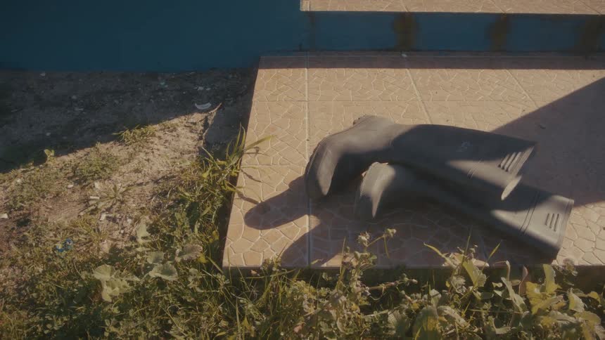 A pair of rainboots lies on a walkway under the sun with grass surrounding the platform