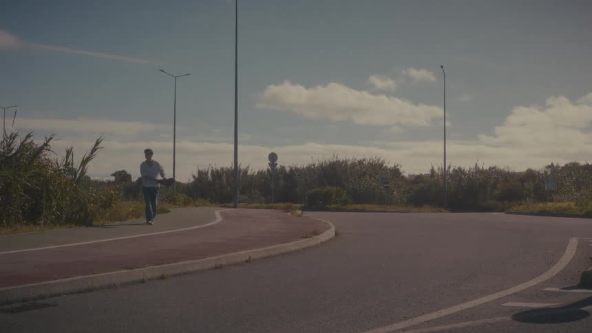 Under a bright clouddotted sky a man walks along a quiet roadside path with a young child perched on his shoulders casually chatting on his phone while navigating the sunny route
