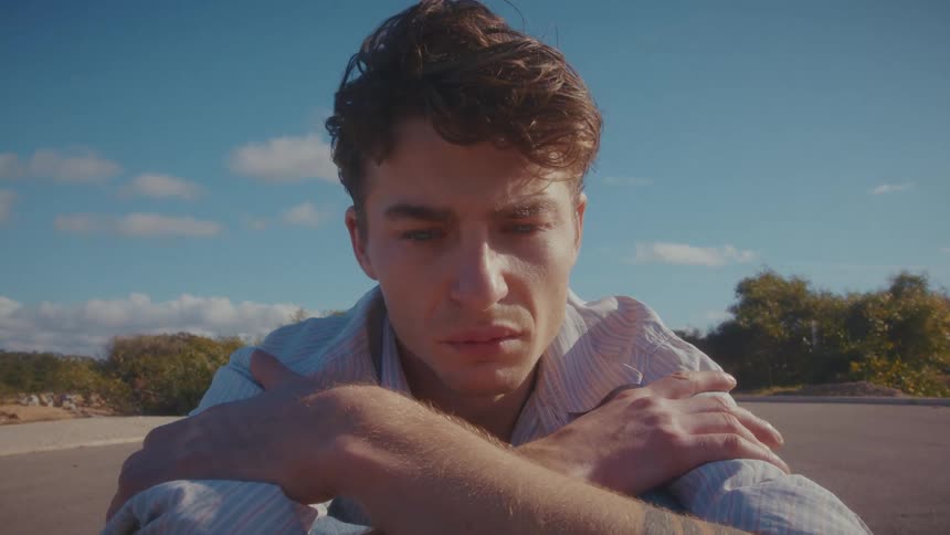 Close up portrait of a young man sitting contemplatively on a road outdoors during daytime