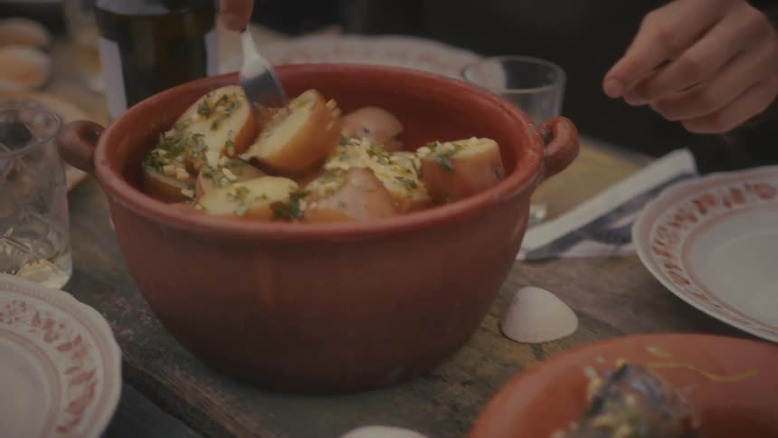 Two people are plating cooked fish and potatoes on a wooden table