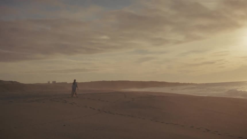Person walking on the beach at dawn near the waterline