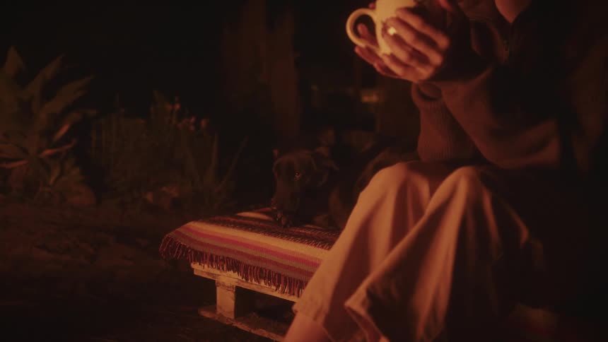 A woman drinks from a mug by her dog