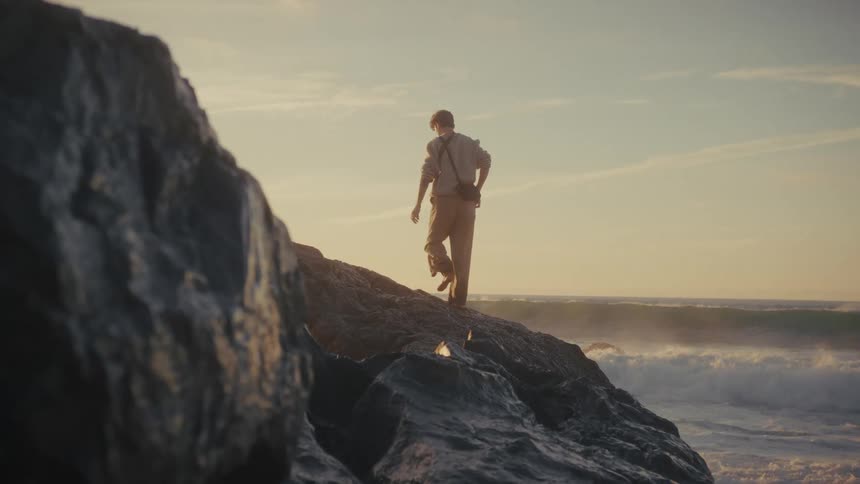 Man climbing on rocks as he walks along the coast and waves splash as they roll in