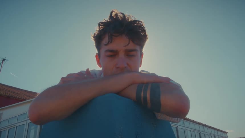 Man leaning on a blue surface with arms crossed under sunlight