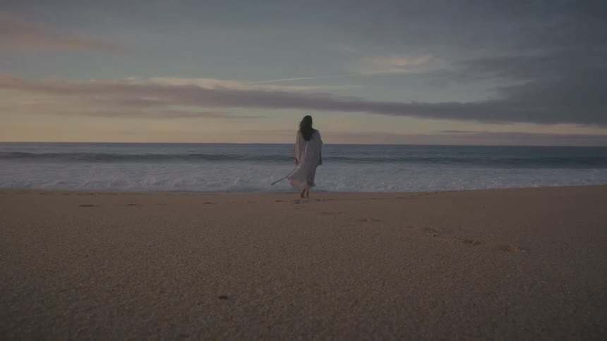 The woman is walking towards the water on the beach