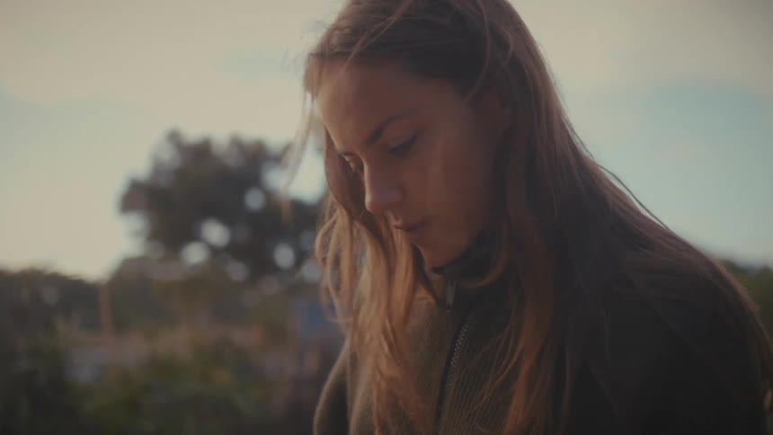 Woman with long hair looks downward in an outdoor setting lit by natural light