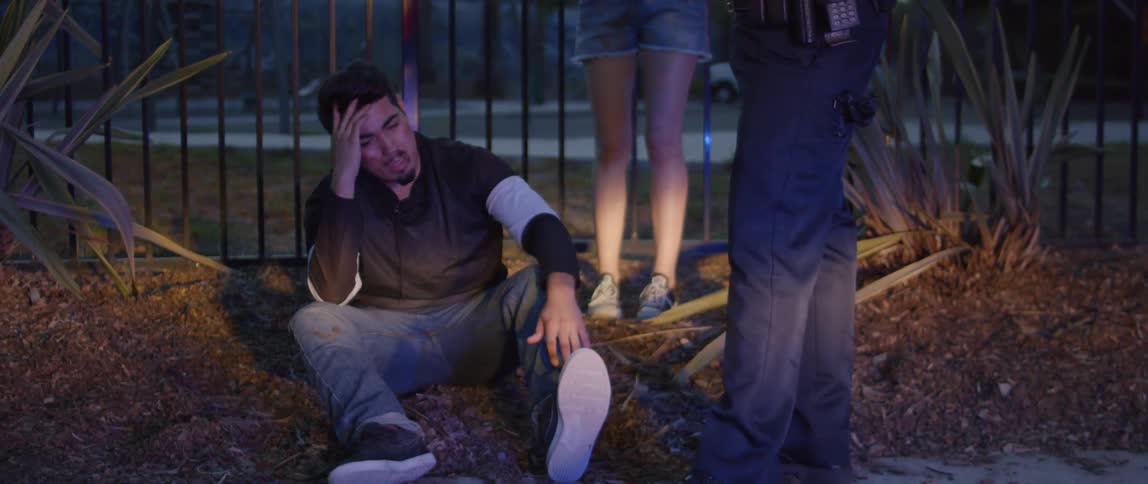 A man is sitting on the ground as a policeman stands near him