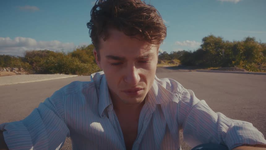 Man sitting on the asphalt with his gaze directed downward in daylight