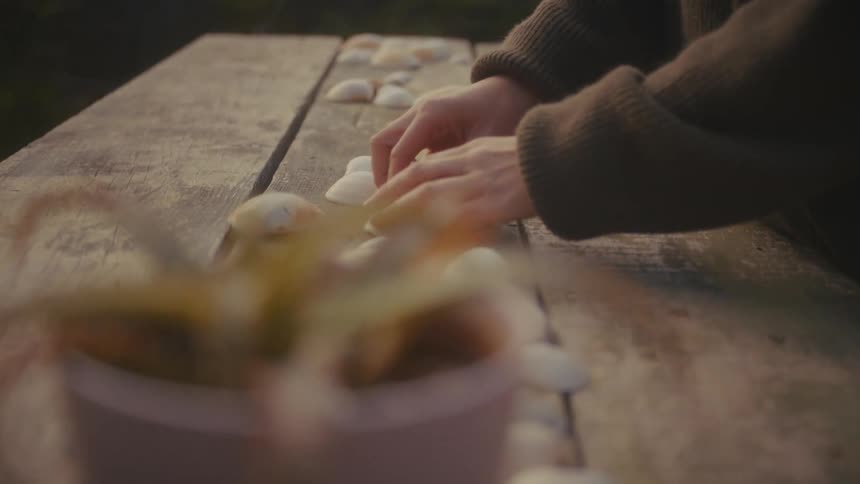 A young woman arranges a series of clam shells on a table outdoors at midday