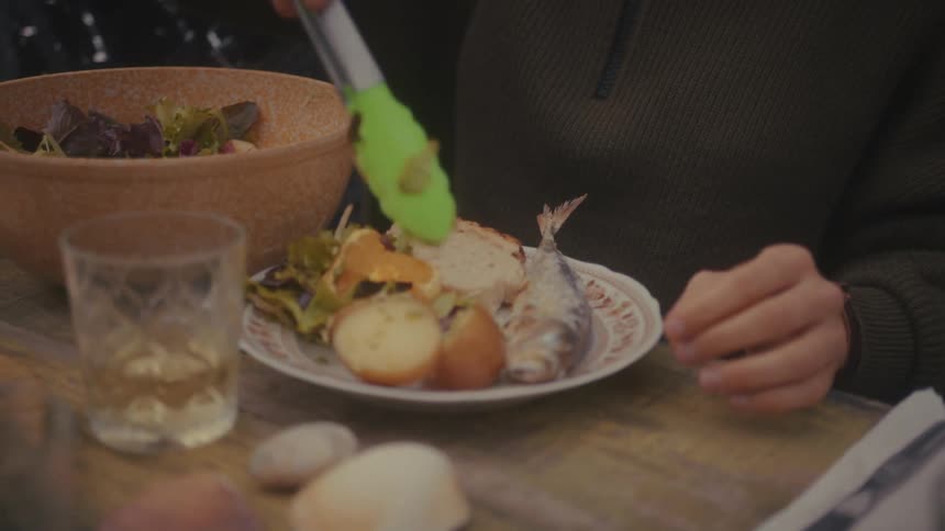 People serving food onto a plate with fish potatoes and salad