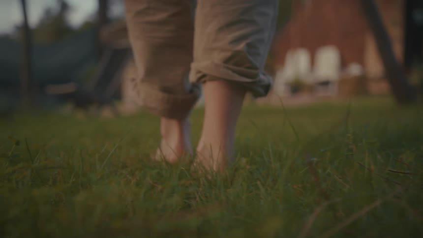 Bare feet walk on grass beside rustic structure