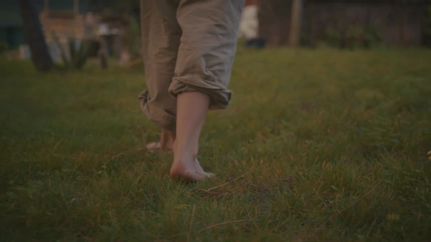 Barefoot person walks across a mowed lawn during the daytime