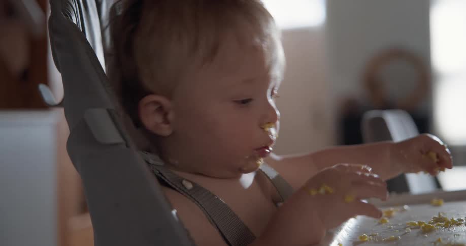 Baby sitting in a high chair holding food with its hands