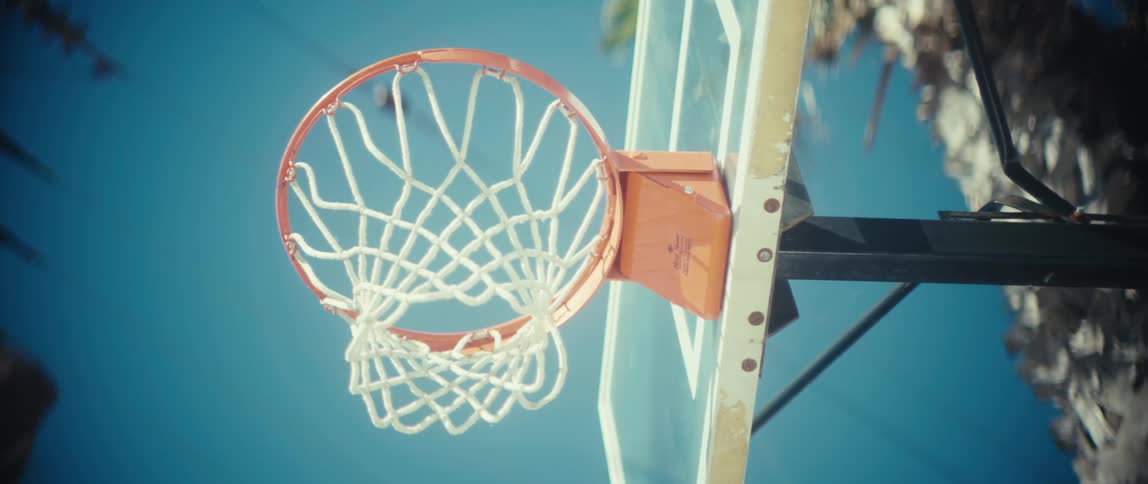 Sunlgiht shines on a basketball hoop and backboard as a player jumps and puts the ball through the hoop